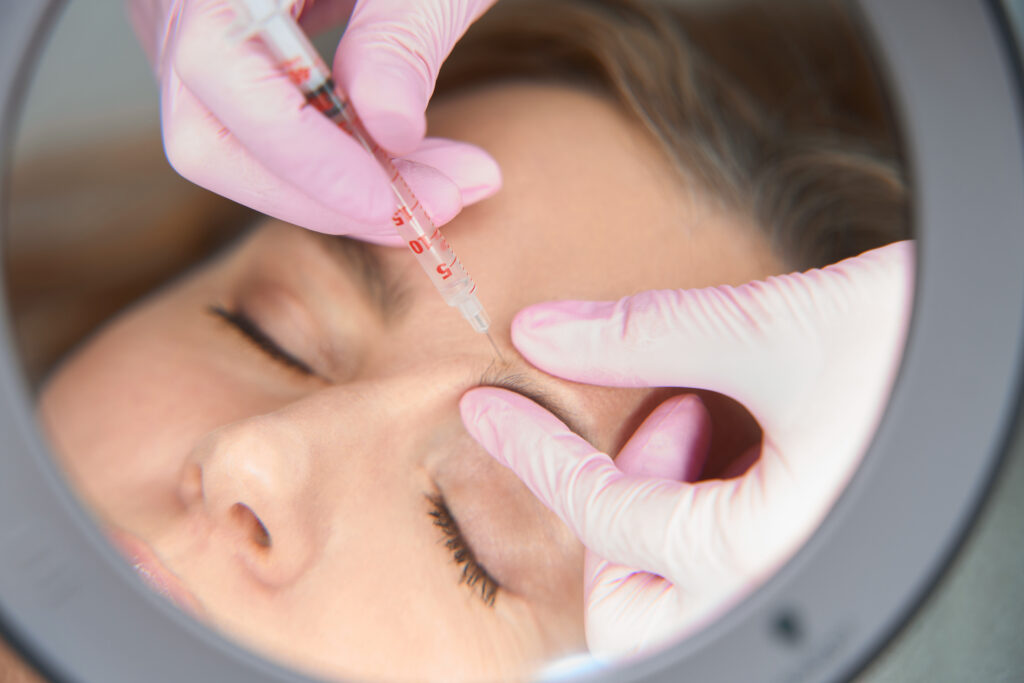 Doctor esthetician makes beauty injections to a blonde woman, the process of the injection procedure is reflected in the mirror